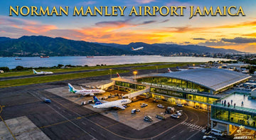 Aerial view of Norman Manley International Airport Jamaica at sunset with terminal, aircraft, runway, mountains, and coastline.