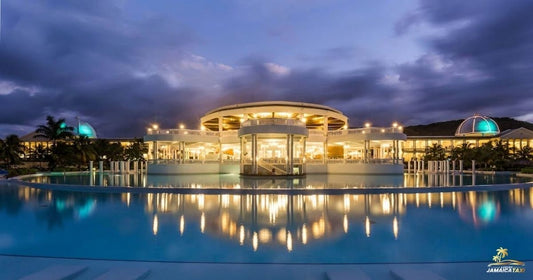 Large illuminated building with a pool reflecting its lights at night